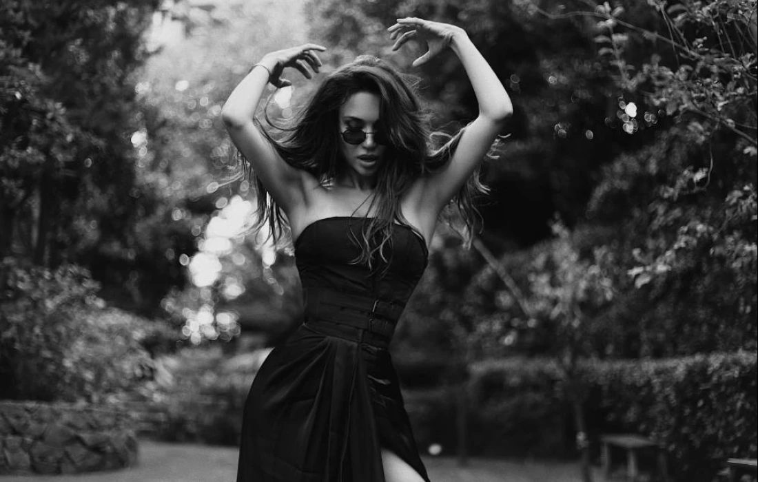 A woman posing in a black dress out in nature 