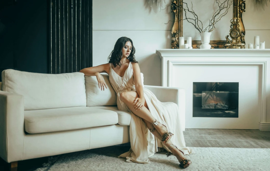 an elegant high class escort in a white dress sitting on a sofa